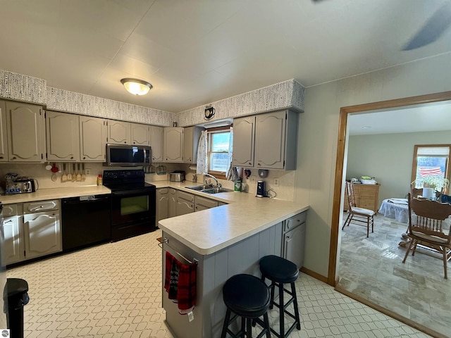 kitchen featuring sink, a kitchen breakfast bar, kitchen peninsula, gray cabinets, and black appliances