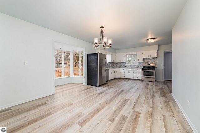 kitchen featuring decorative backsplash, appliances with stainless steel finishes, a notable chandelier, white cabinetry, and hanging light fixtures