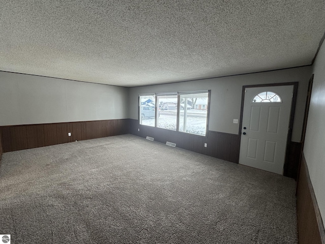 foyer entrance with wood walls, carpet floors, and a textured ceiling