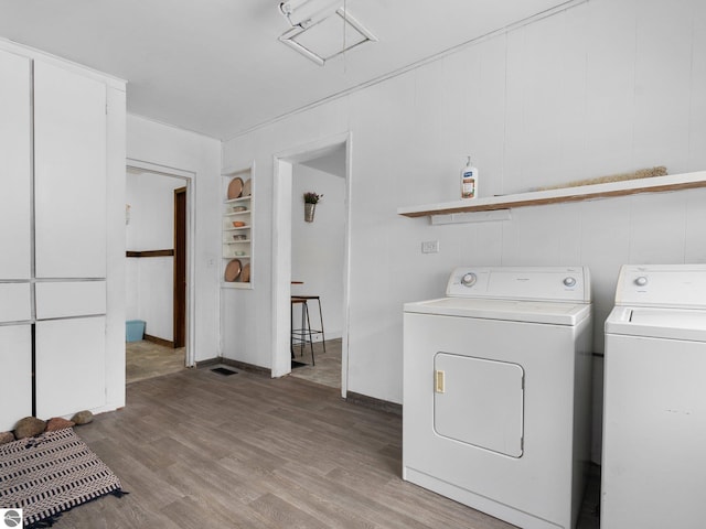 clothes washing area with washer and clothes dryer, built in features, and light hardwood / wood-style flooring