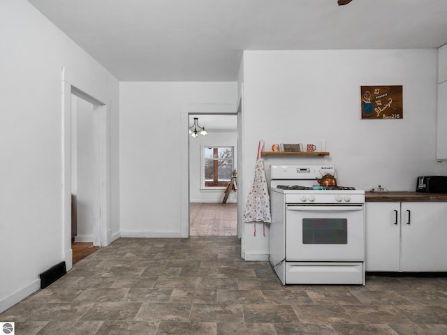 kitchen featuring white gas range, white cabinetry, and a notable chandelier