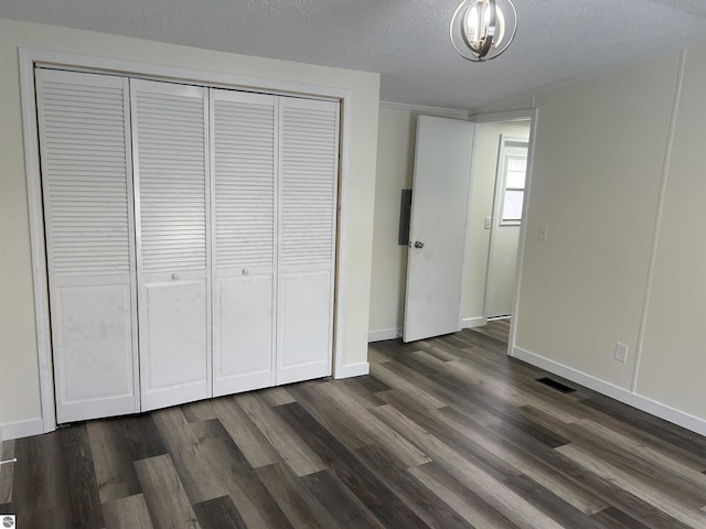 unfurnished bedroom with a chandelier, a closet, dark wood-type flooring, and a textured ceiling