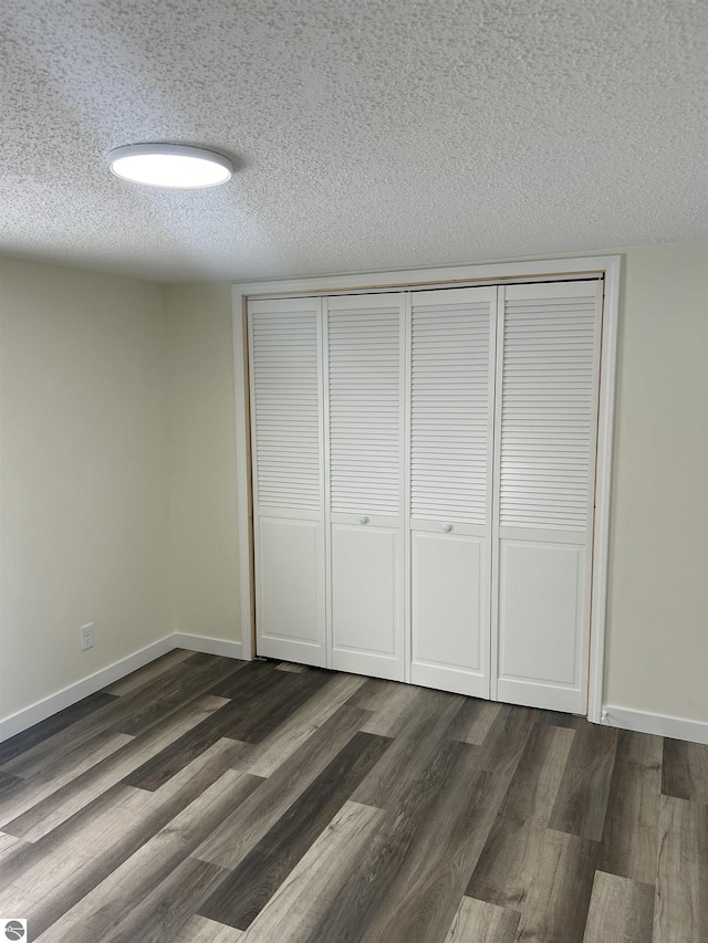 unfurnished bedroom with a textured ceiling, dark hardwood / wood-style floors, and a closet