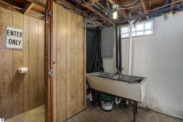 basement with electric panel, wood walls, and sink