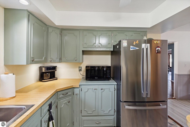 kitchen featuring hardwood / wood-style floors, green cabinets, sink, and stainless steel refrigerator