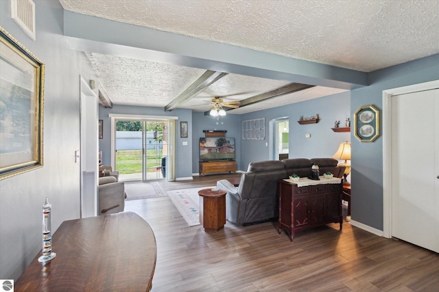 living room featuring beamed ceiling, ceiling fan, wood-type flooring, and a textured ceiling