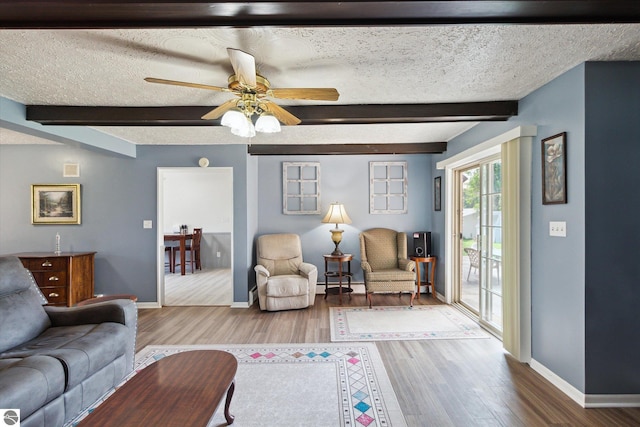 living room featuring beam ceiling, ceiling fan, wood-type flooring, and a textured ceiling