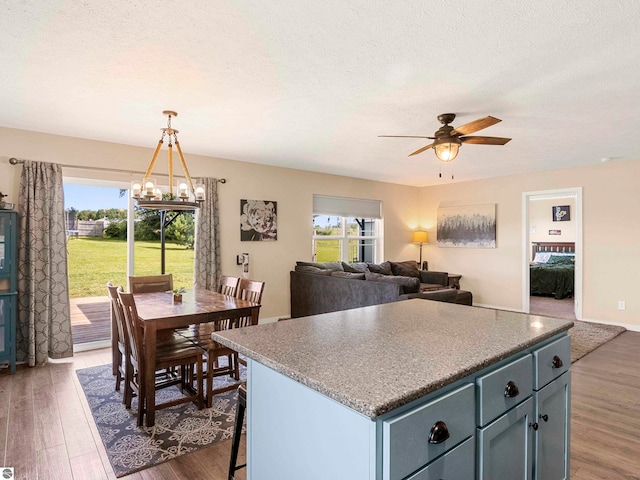 kitchen with ceiling fan with notable chandelier, a textured ceiling, pendant lighting, a center island, and dark hardwood / wood-style floors