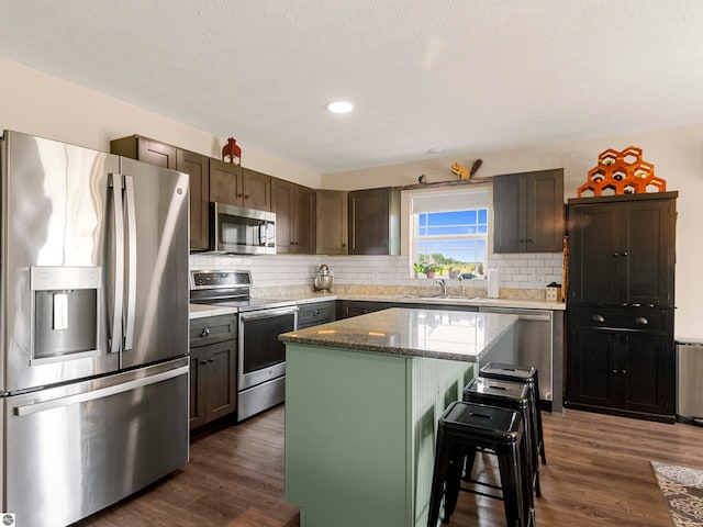 kitchen with a center island, sink, dark stone countertops, dark brown cabinets, and stainless steel appliances