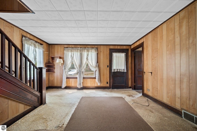 entrance foyer featuring a healthy amount of sunlight, wooden walls, and light colored carpet