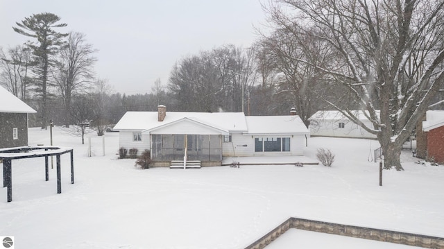 snow covered rear of property featuring a sunroom