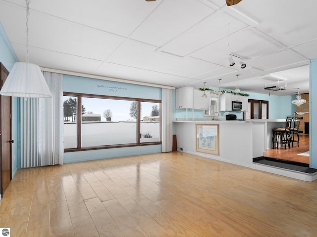 unfurnished living room with light hardwood / wood-style floors, sink, and an inviting chandelier