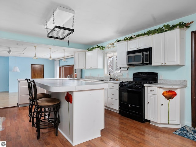 kitchen featuring white cabinets, black gas range, a kitchen island, and hanging light fixtures