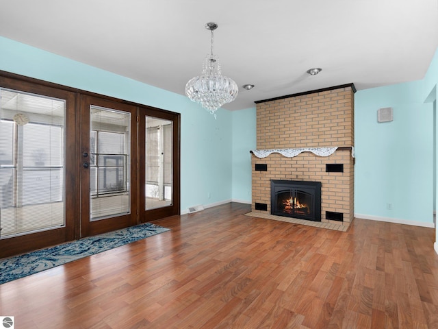 unfurnished living room featuring hardwood / wood-style floors, an inviting chandelier, a fireplace, and french doors