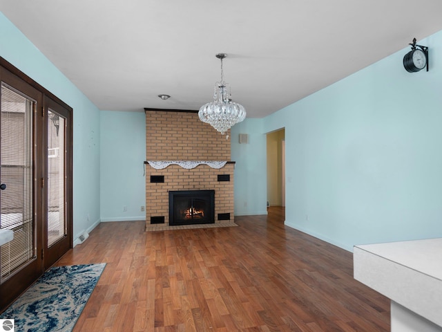 unfurnished living room featuring hardwood / wood-style flooring, a notable chandelier, and a brick fireplace