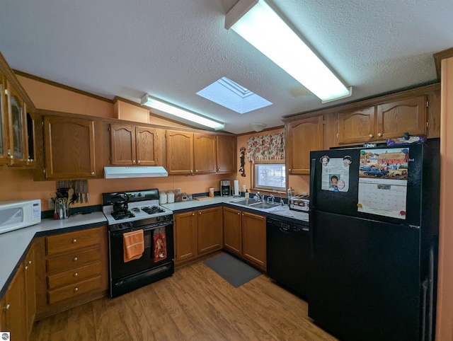 kitchen featuring lofted ceiling with skylight, black appliances, sink, light hardwood / wood-style flooring, and a textured ceiling