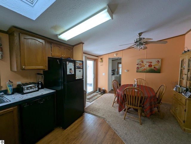 kitchen with lofted ceiling with skylight, black appliances, light hardwood / wood-style flooring, a textured ceiling, and washing machine and clothes dryer