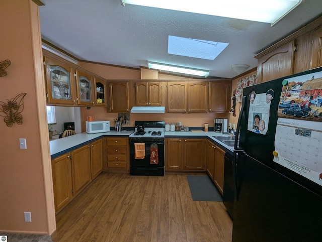 kitchen featuring sink, lofted ceiling with skylight, a textured ceiling, black appliances, and light wood-type flooring