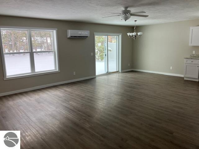 interior space featuring a textured ceiling, ceiling fan with notable chandelier, dark hardwood / wood-style floors, and a wall mounted air conditioner