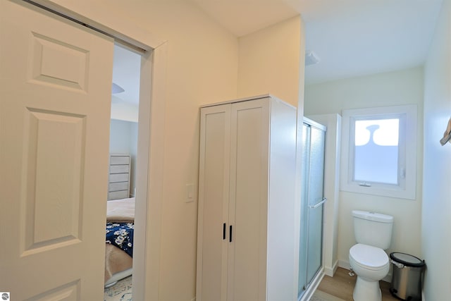 bathroom featuring hardwood / wood-style flooring, a shower with door, and toilet