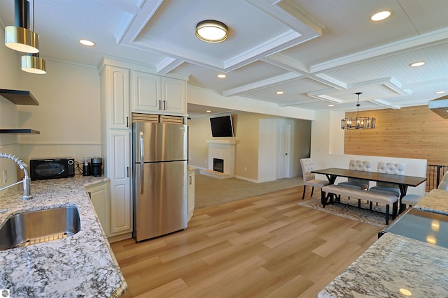 kitchen featuring light stone countertops, sink, white cabinetry, hanging light fixtures, and stainless steel refrigerator