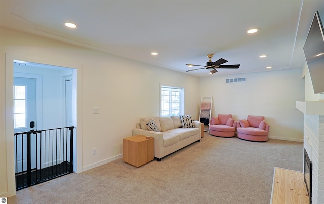 living room featuring ceiling fan, a fireplace, and light colored carpet