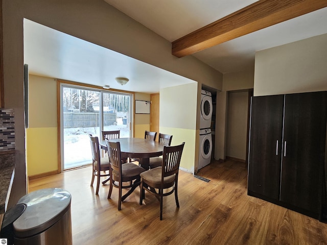 dining space with beam ceiling, stacked washing maching and dryer, and light wood-type flooring