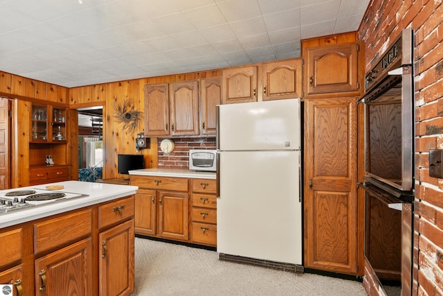 kitchen with brick wall, white appliances, wood walls, light countertops, and brown cabinets