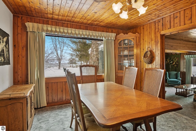 dining room with wooden ceiling, wood walls, a chandelier, and light colored carpet