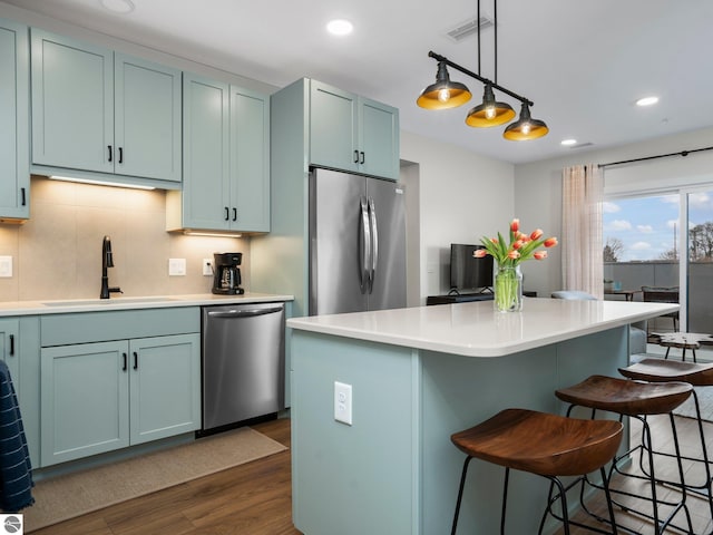 kitchen featuring backsplash, stainless steel appliances, dark wood-type flooring, sink, and hanging light fixtures