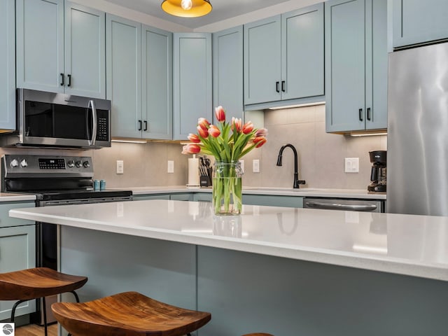 kitchen featuring a kitchen bar, blue cabinets, stainless steel appliances, and tasteful backsplash