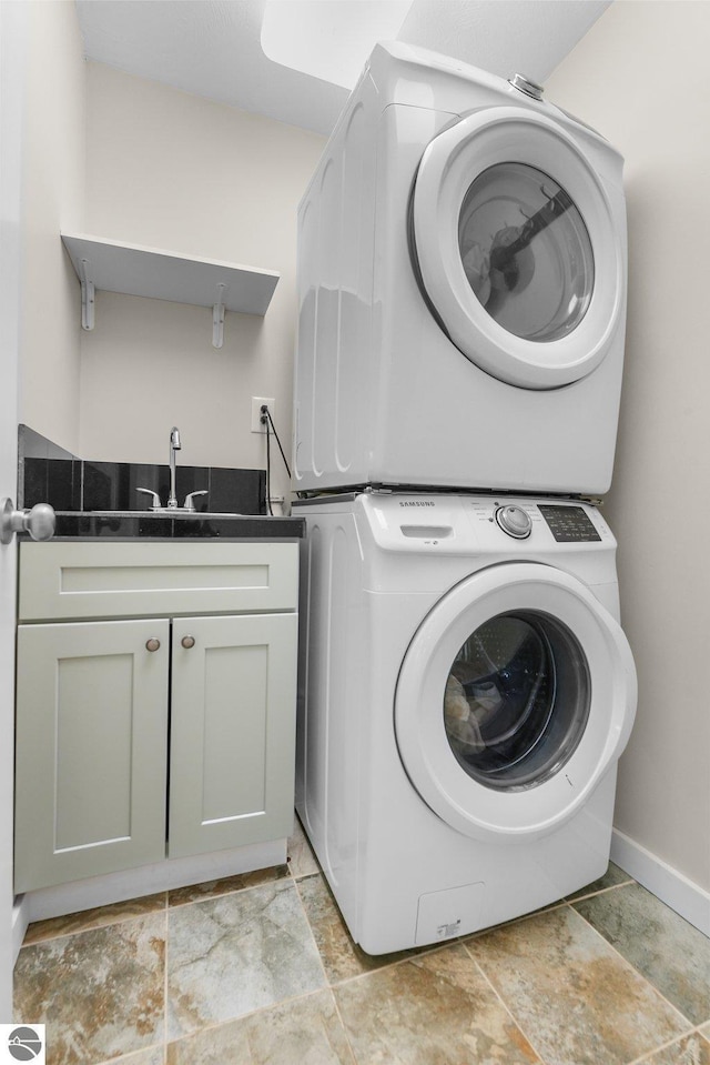 clothes washing area with stacked washer / drying machine, cabinets, and sink