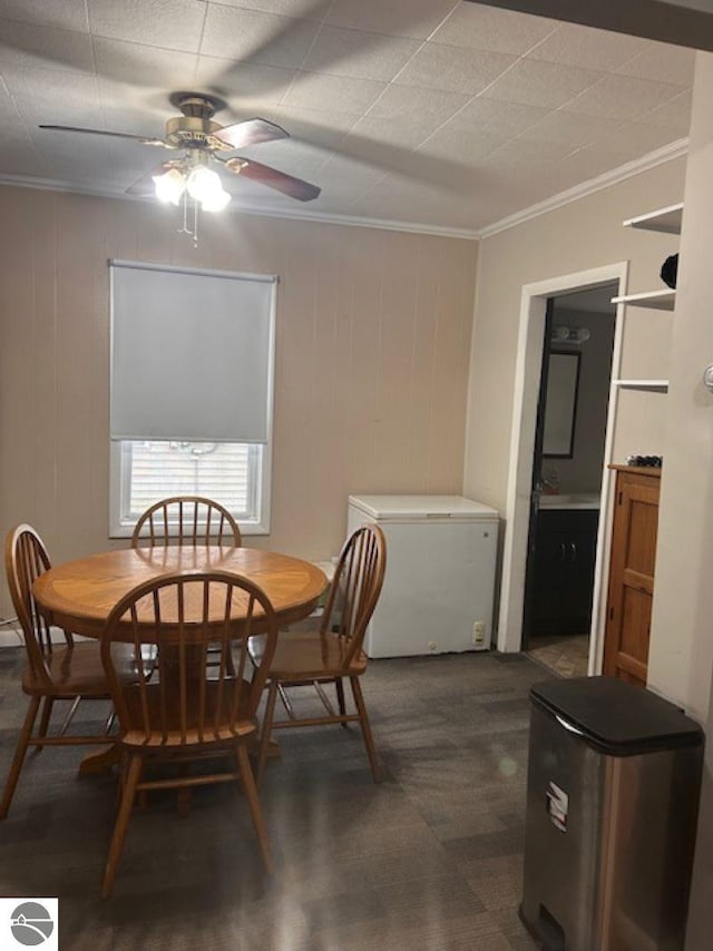 carpeted dining room with ceiling fan, wooden walls, and ornamental molding