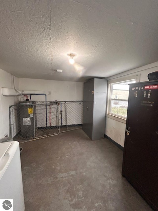 basement with water heater, a textured ceiling, and washer / dryer