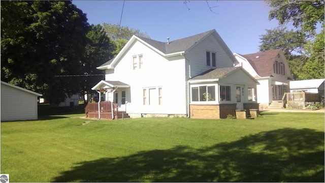 rear view of property featuring a wooden deck, a sunroom, and a lawn