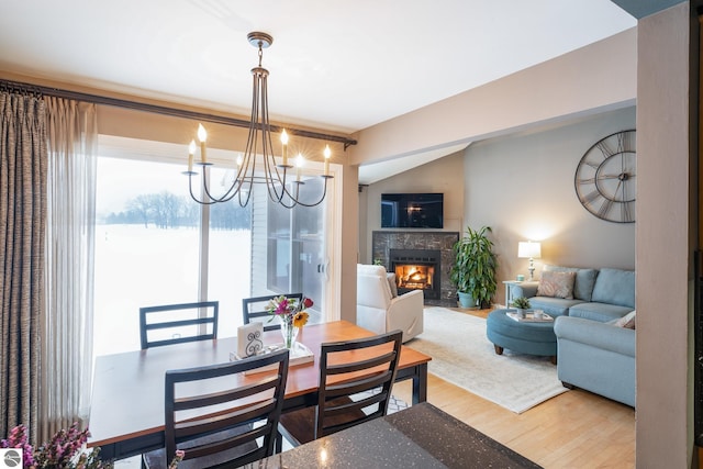 dining area featuring hardwood / wood-style flooring, vaulted ceiling, a fireplace, and a chandelier