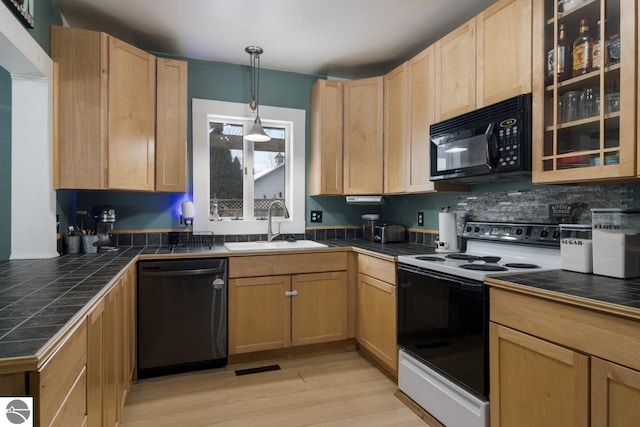 kitchen with tile counters, light wood-type flooring, black appliances, sink, and pendant lighting