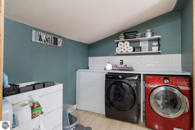 clothes washing area with light hardwood / wood-style flooring, washer and dryer, and a textured ceiling