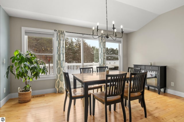 dining space with light wood-type flooring, an inviting chandelier, and vaulted ceiling