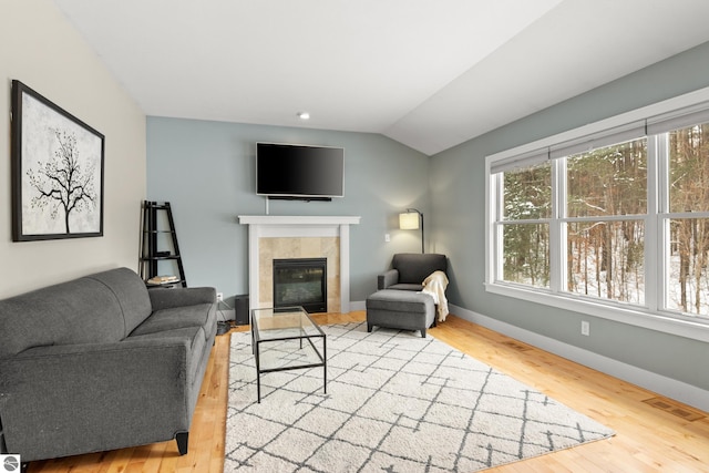 living room with a tile fireplace, vaulted ceiling, and light hardwood / wood-style flooring