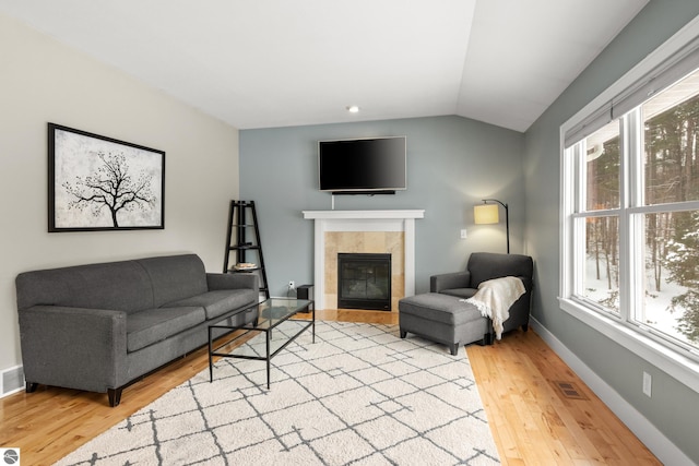 living room with a tile fireplace, vaulted ceiling, and light hardwood / wood-style flooring