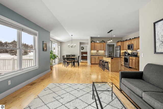 living room featuring light hardwood / wood-style floors, vaulted ceiling, a chandelier, and sink