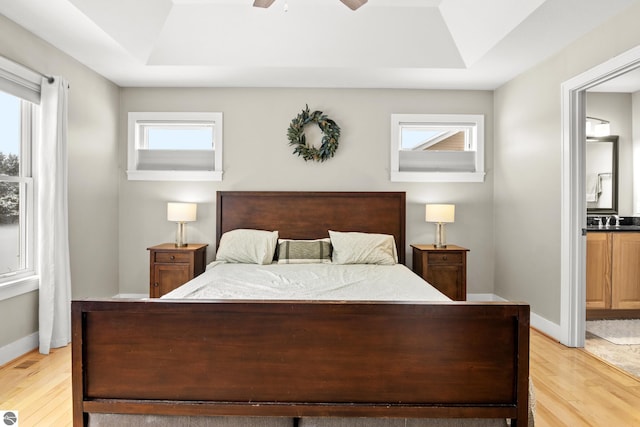 bedroom featuring sink, ceiling fan, a tray ceiling, and light hardwood / wood-style flooring