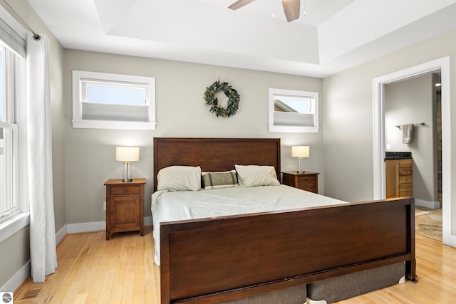 bedroom with ensuite bath, ceiling fan, light hardwood / wood-style floors, and a raised ceiling