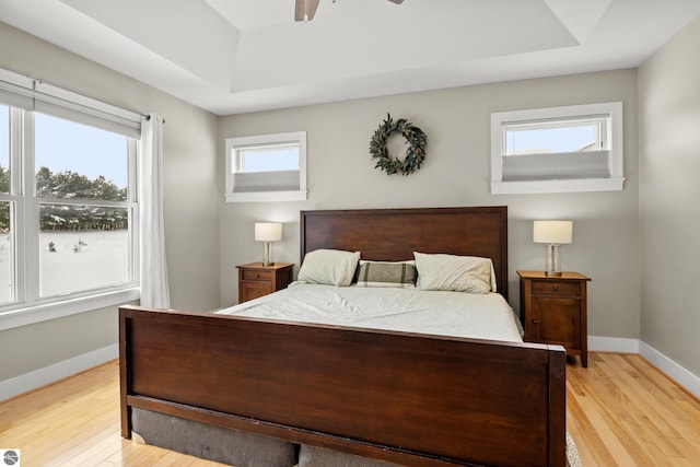 bedroom featuring ceiling fan, multiple windows, light hardwood / wood-style floors, and a raised ceiling