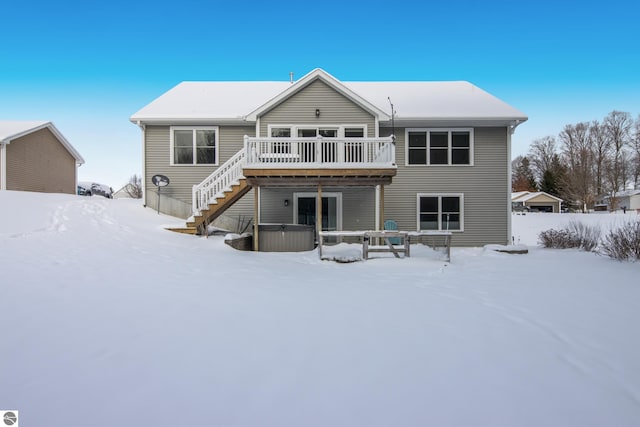 snow covered rear of property featuring a deck and a hot tub