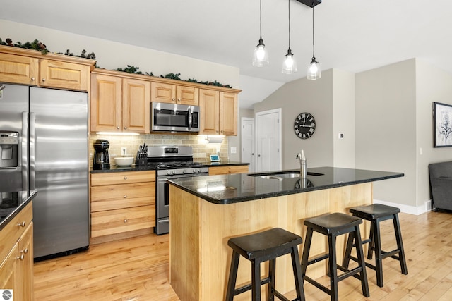 kitchen featuring stainless steel appliances, a kitchen island with sink, light hardwood / wood-style floors, and dark stone countertops