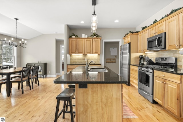 kitchen with appliances with stainless steel finishes, hanging light fixtures, an inviting chandelier, and a center island with sink