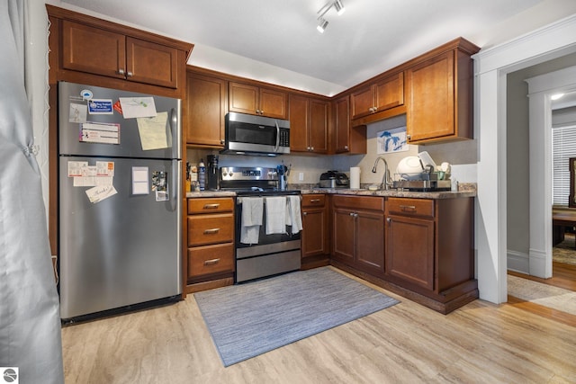 kitchen featuring appliances with stainless steel finishes, light wood-type flooring, dark stone counters, and sink