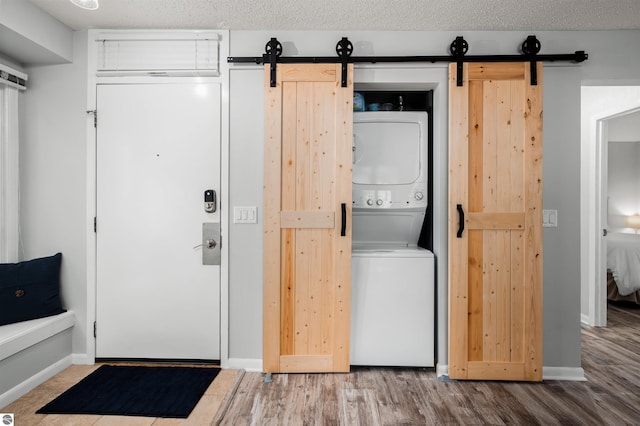 laundry area featuring a barn door, stacked washer and clothes dryer, and hardwood / wood-style floors